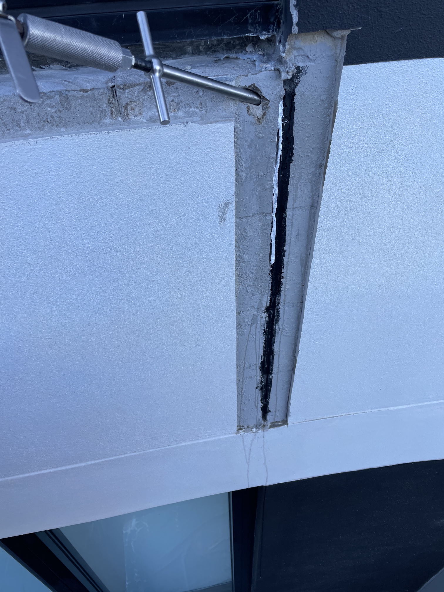 Window Construction Joint, with SNSeal Injectable sealant being injected into joint. Can see white rubber spilling down from injection point.